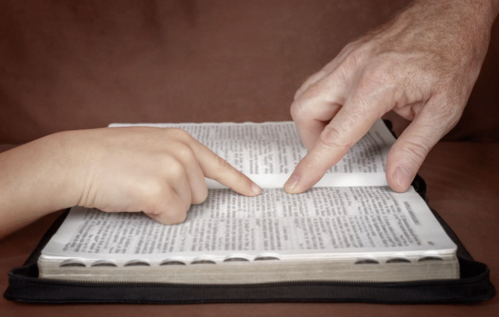 two hands pointing to bible verses in an open bible 